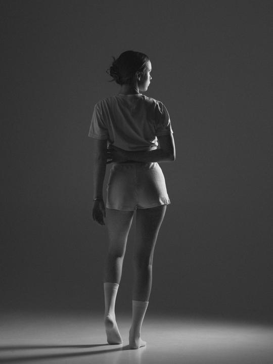 A woman stands with her back to the viewer, looking over her shoulder in a black and white portrait.