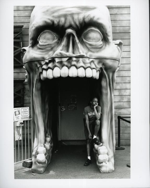 A man sits in the mouth of a giant skull sculpture.