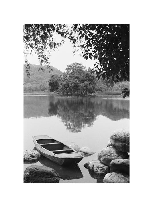 A small boat floats in a lake surrounded by rocks and trees, with a small island in the distance.