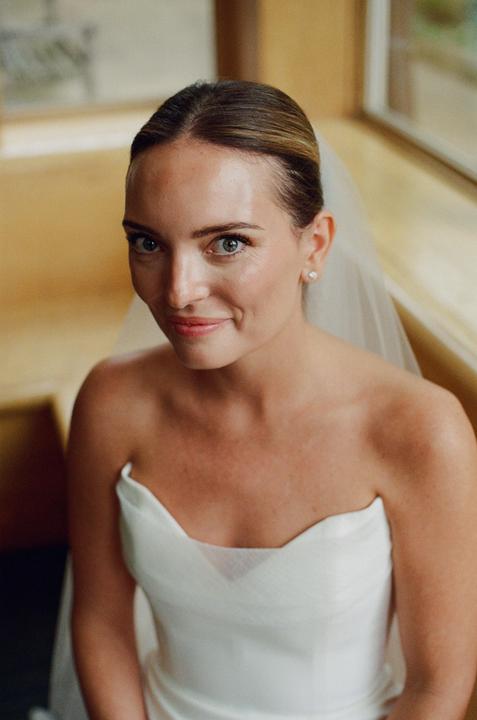 A woman in a white dress and veil looks directly at the viewer.