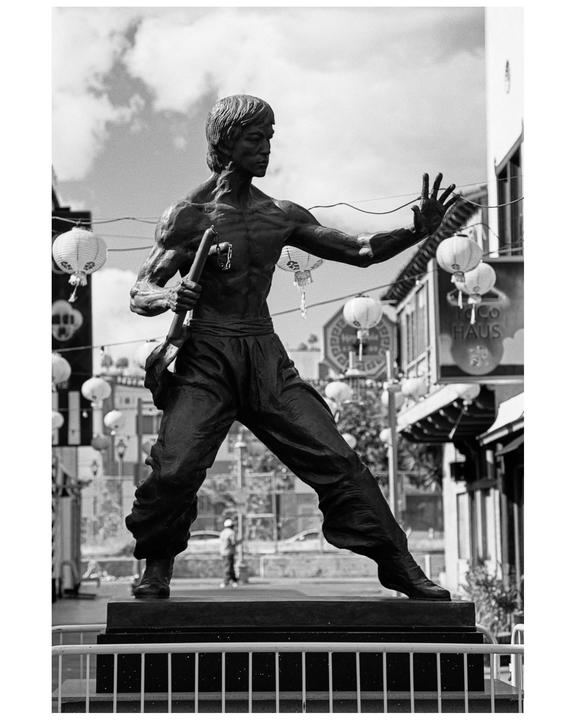A statue of a martial artist in an action pose stands on a pedestal in a city street decorated with paper lanterns.