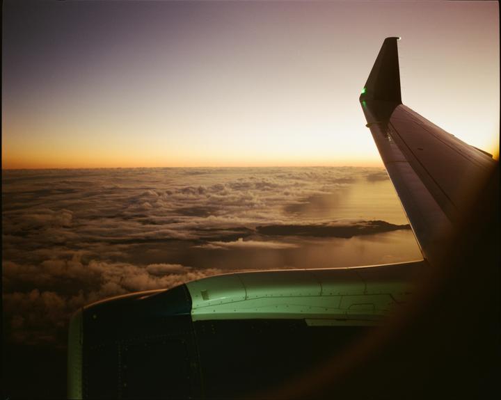 An airplane wing is visible above a layer of clouds during sunset.