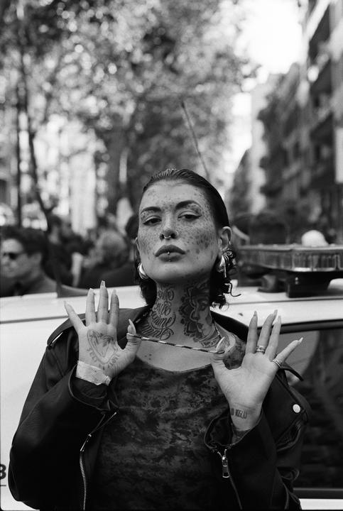 A woman with tattoos on her neck and face holds a necklace with both hands.