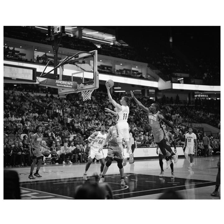 A basketball player in a white jersey jumps to shoot a basketball while an opposing player in a dark jersey jumps to block him.
