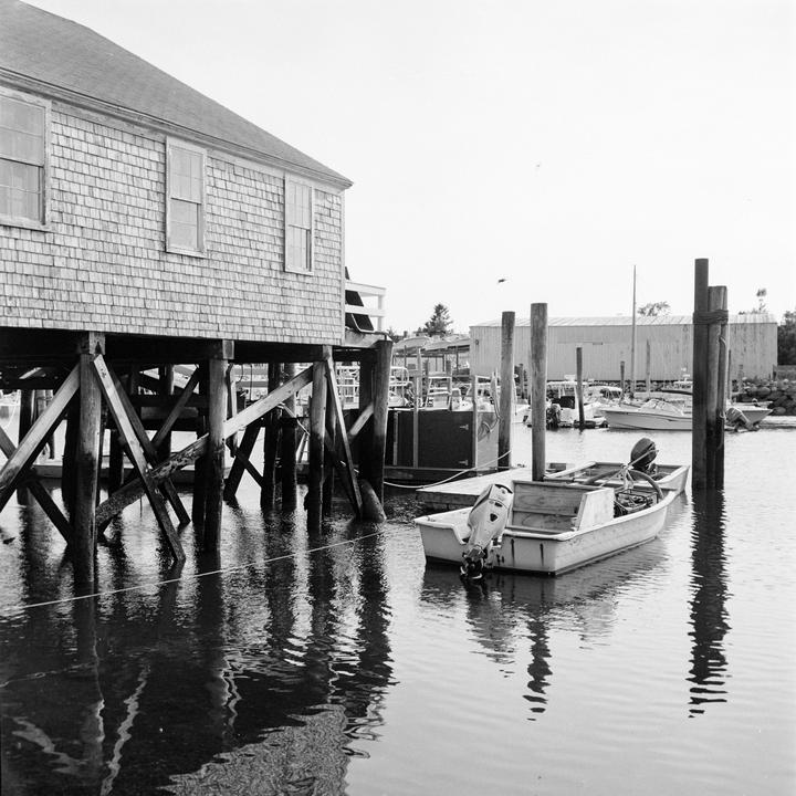 A small boat is moored next to a wooden building on stilts over the water.