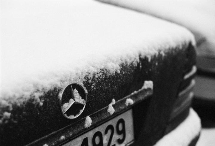 The back of a car is covered in snow, with a Mercedes-Benz emblem and a license plate visible.