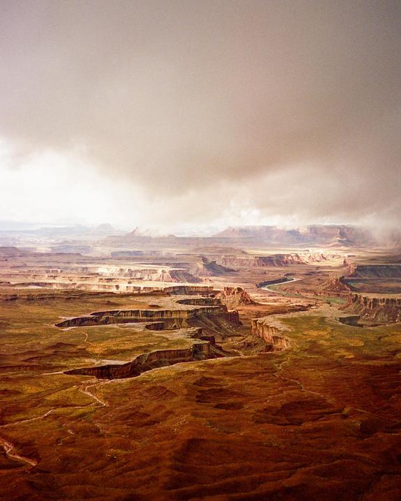 A vast canyon landscape with a river winding through it is visible under a cloudy sky.