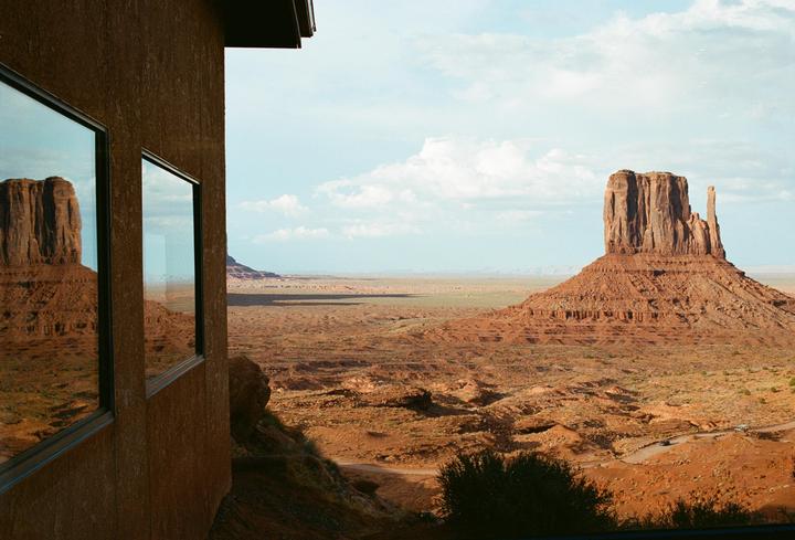 A large rock formation is reflected in the windows of a building overlooking a desert landscape.