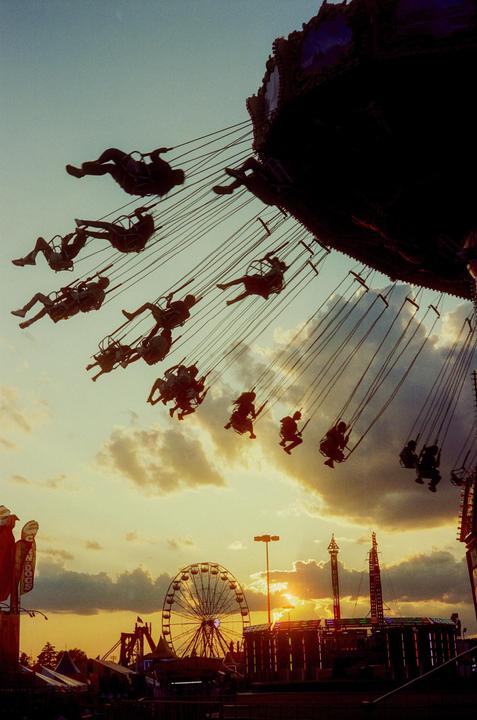 People ride a swing carousel and a ferris wheel at a fairground during sunset.