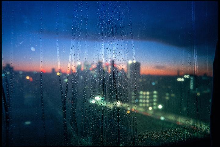 Raindrops cover a window looking out at a city skyline at dusk.