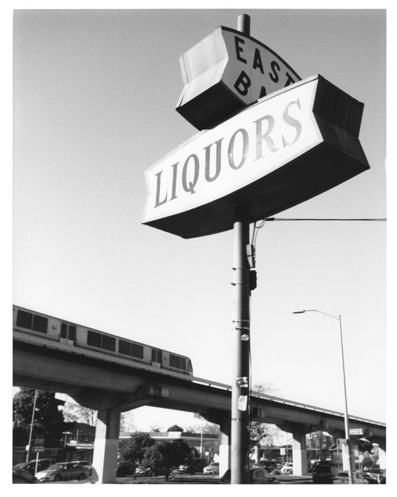 A liquor store sign stands tall with a train on an elevated track passing behind it.