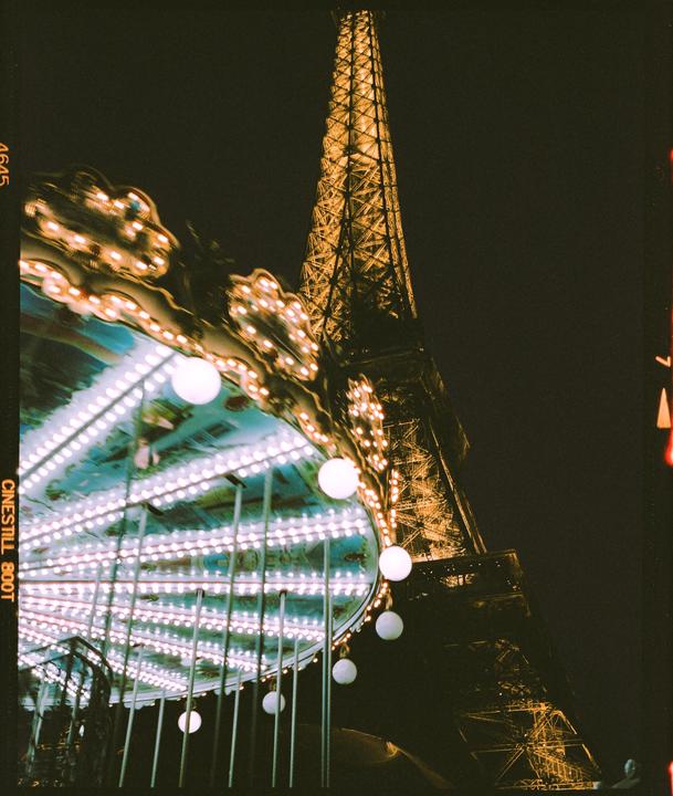 A brightly lit carousel is in the foreground with the illuminated Eiffel Tower in the background at night.
