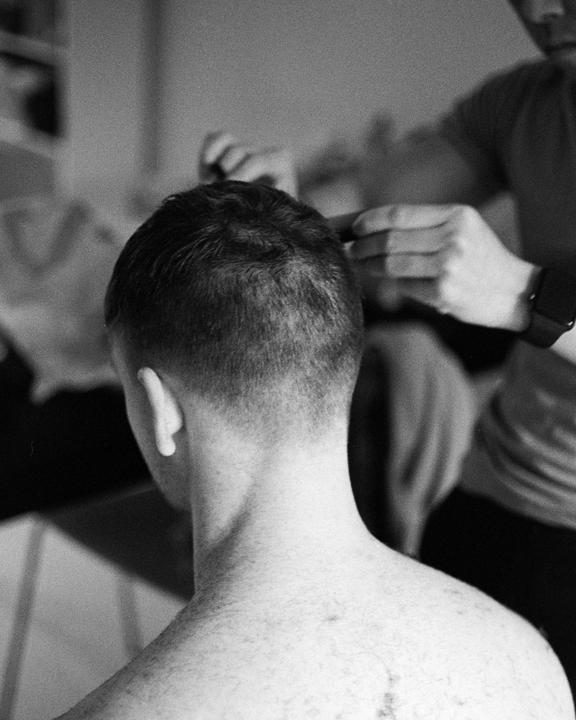 A man receives a haircut from behind, with another person's hands visible.