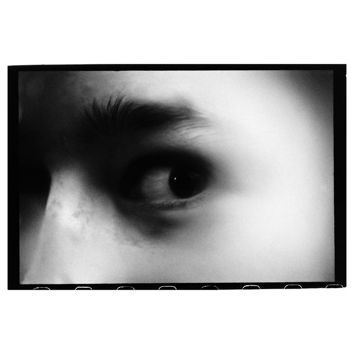 A close-up, black and white portrait shows a person's eye and eyebrow.