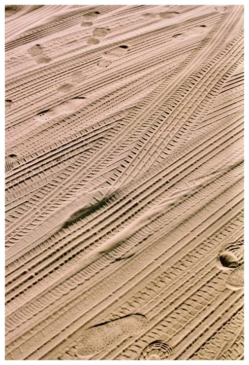 Tire tracks and footprints are visible in the sand.
