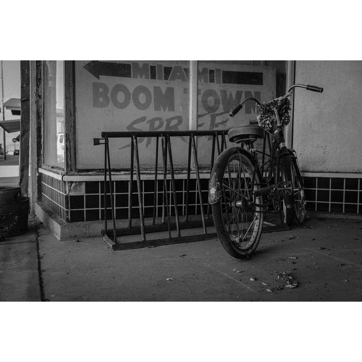 A bicycle is parked next to a bike rack in front of a storefront with a "Miami Boomtown" sign.
