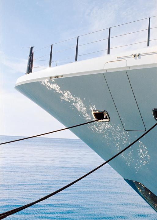 The bow of a white yacht is docked in blue water under a clear sky.