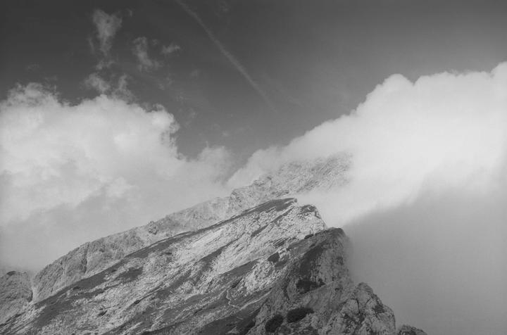 Clouds partially obscure a rocky mountain range under a sky with scattered clouds.