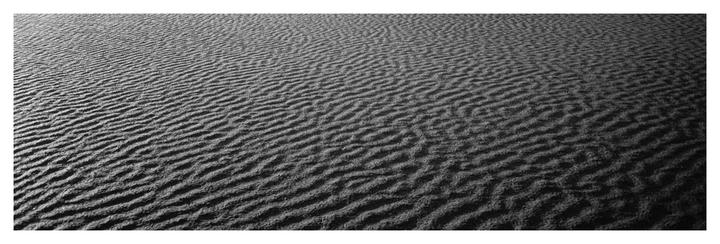 A black and white image shows the rippled texture of sand.