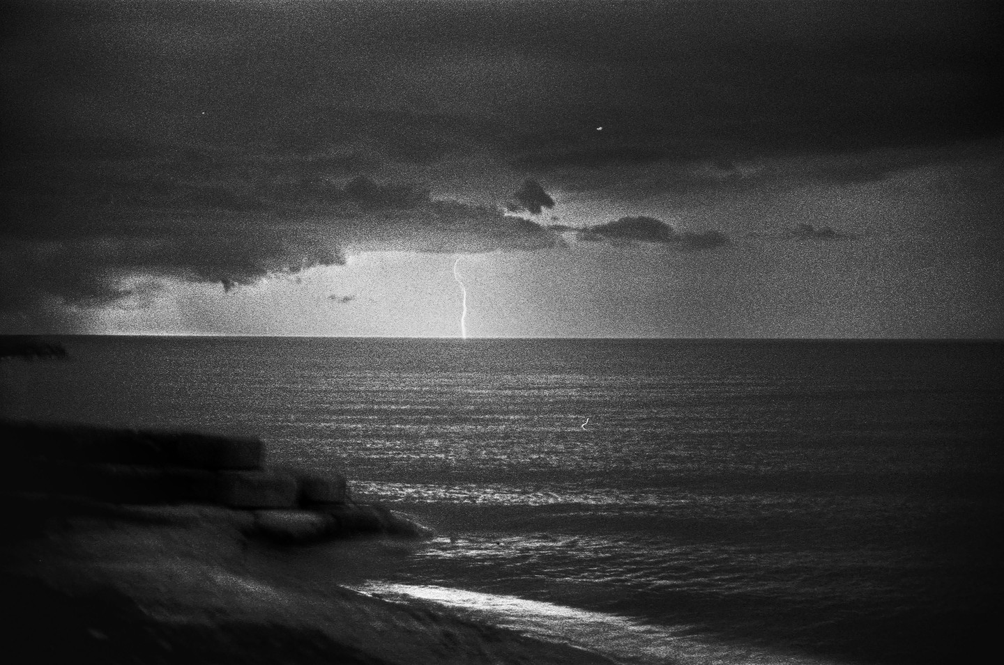 A bolt of lightning strikes the ocean under a dark, cloudy sky.