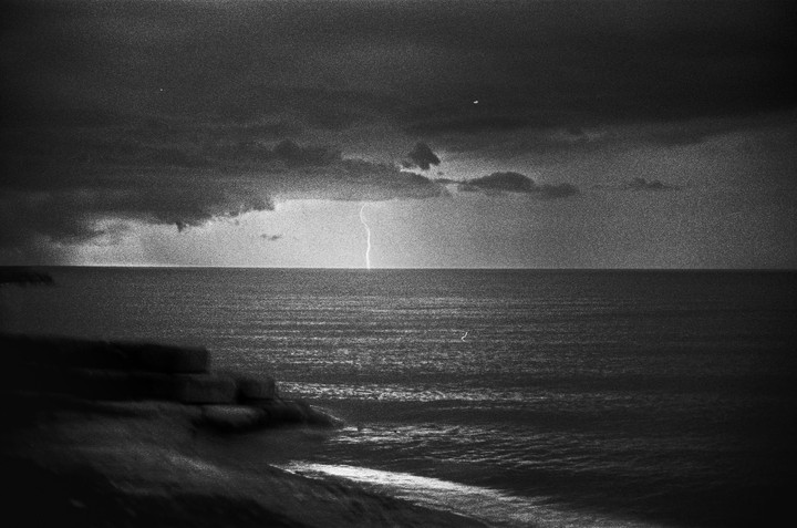 A bolt of lightning strikes the ocean under a dark, cloudy sky.