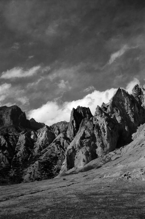 A dramatic black and white landscape shows rugged mountains under a cloudy sky.